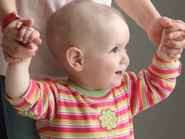 Pequeña niña sosteniendo las manos de su madre, intentando dar sus primeros pasos.