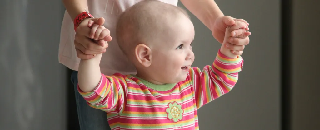 Pequeña niña sosteniendo las manos de su madre, intentando dar sus primeros pasos.